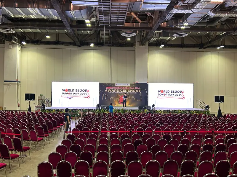 Hall set for an award ceremony, rows of red seats facing three screens