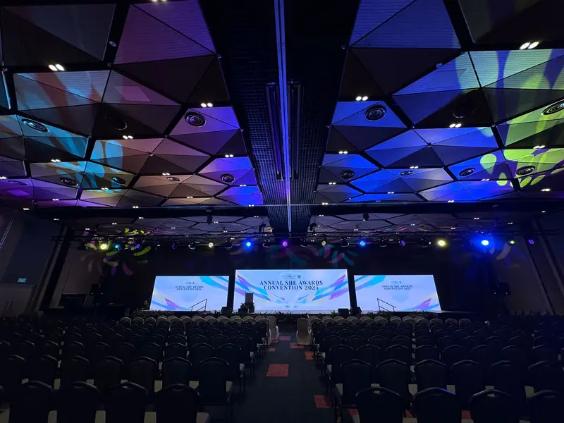 Auditorium before an awards event, coloured light across the ceiling and three screens on stage