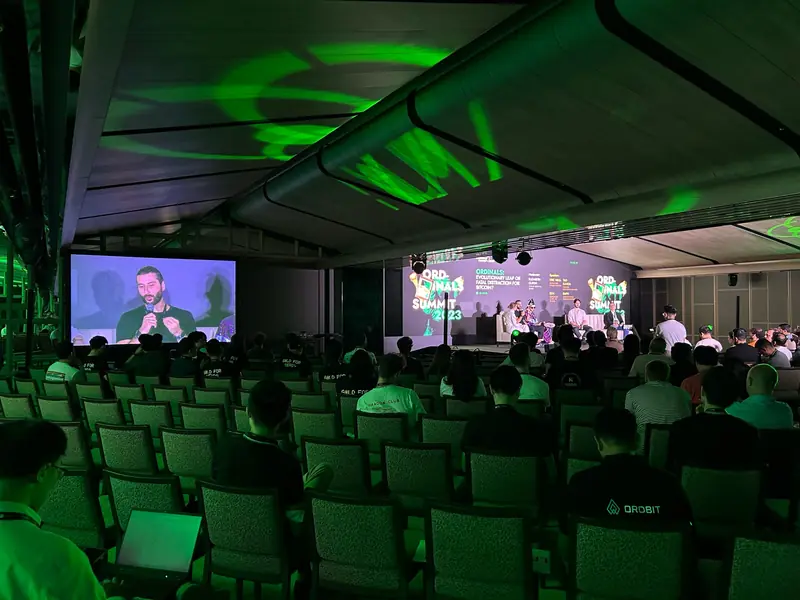 Conference hall lit green, with the speaker shown on a side screen