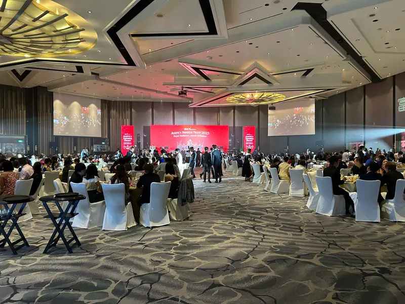 Gala dinner in a ballroom, guests standing between tables in front of a red stage backdrop