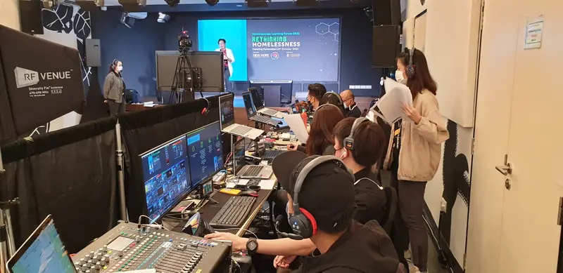 Livestream control table with a vision mixer and monitors, the stage behind