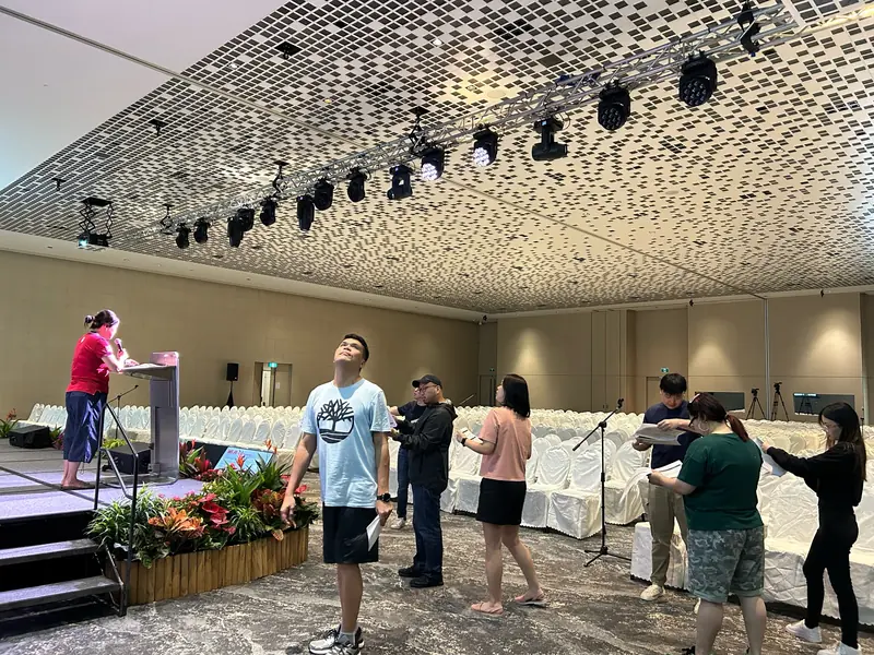 A rehearsal before an event, with a lighting truss above a low stage and a lectern