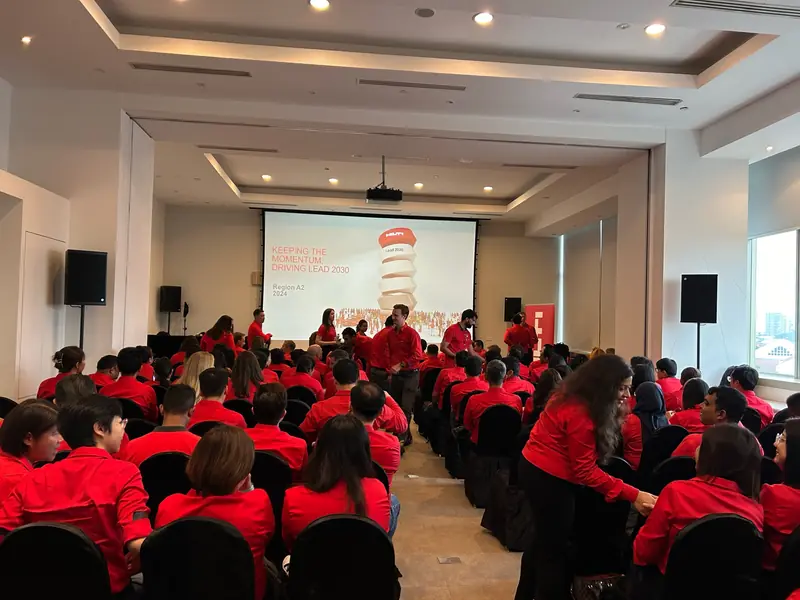 Town hall audience in red shirts facing a projection screen